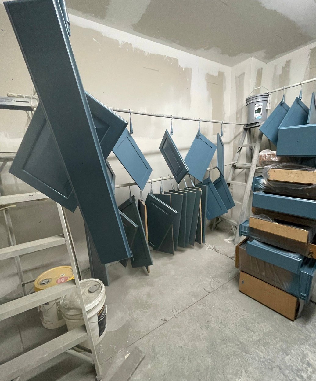 Blue painted cabinet doors hanging to dry in a paint booth